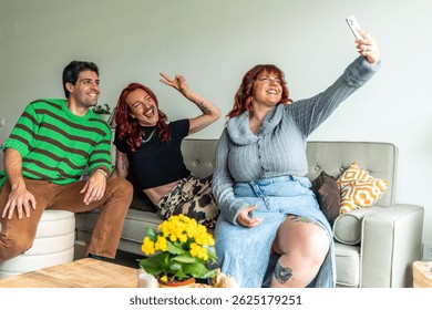 Group of young non-binary and plus-size friends laughing and taking a selfie on a sofa at home, celebrating body positivity and diversity in their friendship