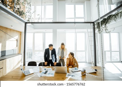 Group Of A Young Office Employees Having Some Office Work At The Large Meeting Table, Wide View On The Spacious Room With Large Windows