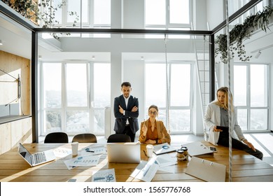 Group Of A Young Office Employees Having Some Office Work At The Large Meeting Table, Wide View On The Spacious Room With Large Windows