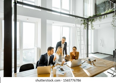 Group Of A Young Office Employees Having Some Office Work At The Large Meeting Table, Wide View On The Spacious Room With Large Windows