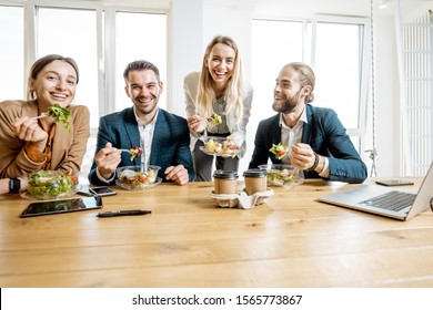 Group Of A Young Office Workers Eating Salads And Drinking Coffee At The Modern Office Canteen. Concept Of A Healthy Takeaway Food On The Work