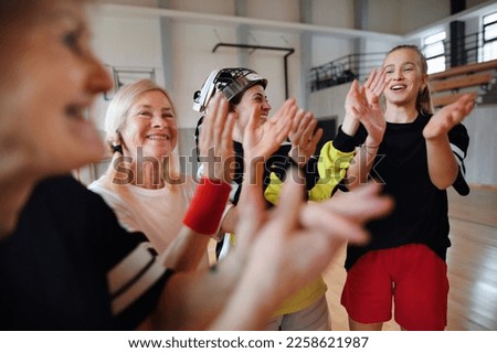 Group of young and old cheerful women, floorball team players, in gym cebrating victory.