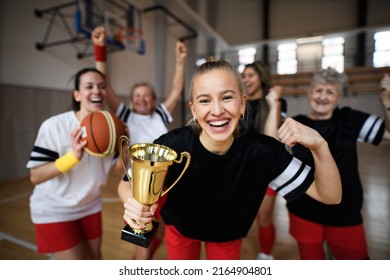 Group Of Young And Old Women, Basketball Team Players, In Gym With Trophy Celebrating Victory.