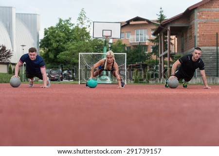 A Group Of Young People In Aerobics Class Performing Push-Ups On Medicine Ball Exercise Outdoor