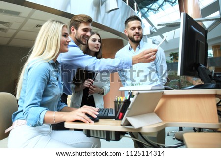 Group of young people in casual wear sitting at the office desk and discussing something while looking at PC together.