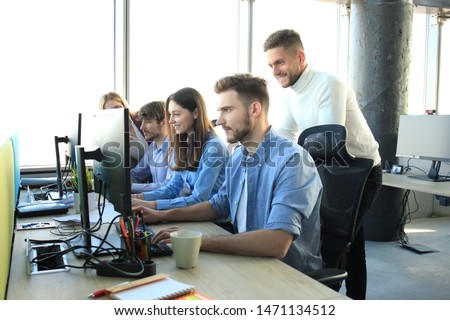 Group of young people in casual wear sitting at the office desk and discussing something while looking at PC together.