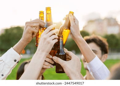 Group of young people clinking beer bottles at summer party. Millennial friends celebrating together at city park. Friendship and beverage concept. - Powered by Shutterstock