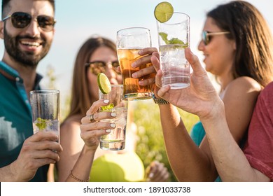 Group of young people clinking cocktail glasses outdoors in the summer. Gathering of friends enjoying time together at outdoors cafe drinking alcoholic drinks