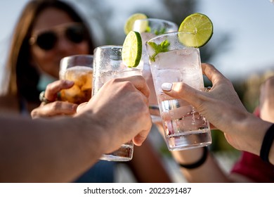 Group of young people clinking cocktail drink glasses toasting. Best friends wearing a lowered face mask having a funny reunion.