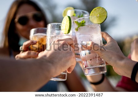 Group of young people clinking cocktail drink glasses toasting. Best friends wearing a lowered face mask having a funny reunion.