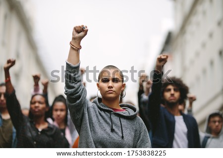 Group of young people demonstrating against the government on the road with their raised fists. Multi-ethnic people protesting on the street.