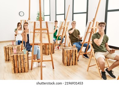 Group Of Young People Drawing At Art Studio Covering Mouth With Hand, Shocked And Afraid For Mistake. Surprised Expression 