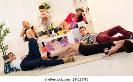 A Group Of Young People, Drunk And Hungover After House Party. A Young Man Leaning On Guitar, Sitting On The Couch Between Hungover Girls. On The Floor Lay Two Boys And One Girl.