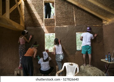 A Group Of Young People Earth Plastering The Wall Of House.