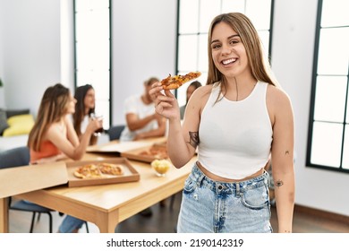 Group Of Young People Eating Italian Pizza Sitting On The Table At Home. Woman Standing And Holding Portion.