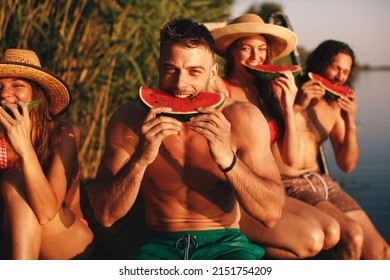 Group of young people eating watermelon on a dock by the river during the summer sunny day - Shutterstock ID 2151754209