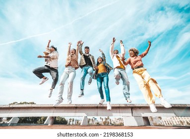 Group of young people enjoying freedom together - Happy multicultural friends jumping on city street - Happiness concept with guys and girls raising arms up to the sky