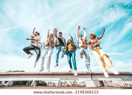 Group of young people enjoying freedom together - Happy multicultural friends jumping on city street - Happiness concept with guys and girls raising arms up to the sky