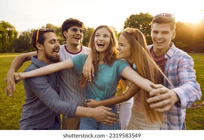 Group of young people enjoying summer, meeting in the park and having fun together. Cheerful pretty girl makes a funny, happy face when a bunch of her friends hug her all together. Friendship concept - Powered by Shutterstock