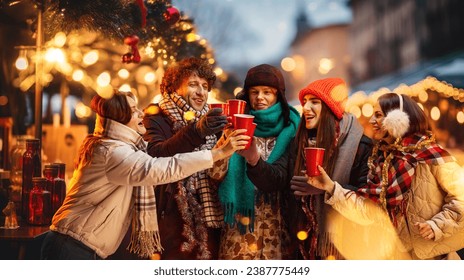 Group of young people, friends walking on cozy winter evening on street fair, drinking mulled wine, tea. Unfocused street. Concept of winter holidays, Christmas, traditions, outdoor fair, happiness - Powered by Shutterstock