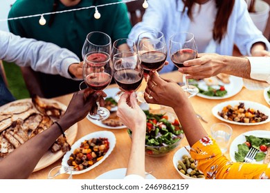 Group of young people hands toasting red wine at rooftop party. Multiracial friends celebrating at bbq dinner at home garden. - Powered by Shutterstock