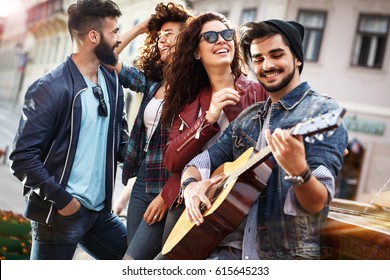 Group Of Young People Hangout  On Street In Downtown.They Standing By The City Square,drinking And Playing Guitar.