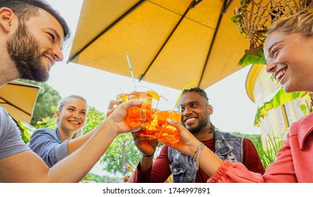 Group of young people having fun outside in a bar with drinks in summer - Friends cheering with coktail and smiling laughing with each other 