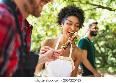 Group of young people having fun in the park at barbecue grilling and eating meat skewers together - Shutterstock ID 2054220485
