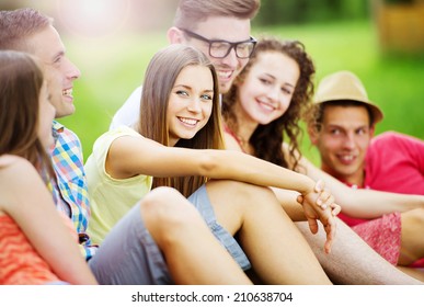 Group Of Young People Having Fun In Park, Sitting On The Grass