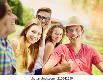 Group Of Young People Having Fun In Park, Sitting On The Grass