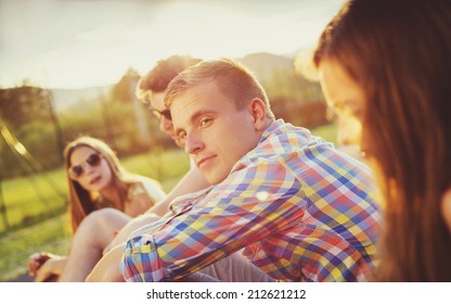 Group Of Young People Having Fun In Park, Sitting On The Grass