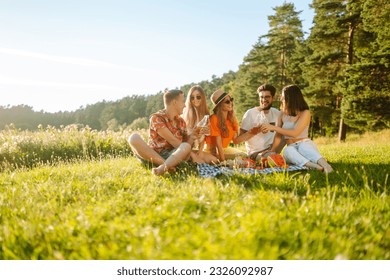 Group of young people  having fun while drinking beer,  talking at picnic party outside city on warm summer day. Vacation, picnic, friendship or holliday concept. - Powered by Shutterstock