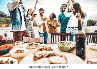 Group of young people having fun drinking red wine on balcony rooftop bbq dinner party - Happy multiracial friends eating barbecue food at restaurant terrace - Food and drink life style concept  - Powered by Shutterstock