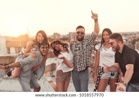 Group of young people having fun at a summertime rooftop party, at sunset. Focus on the people in the middle
