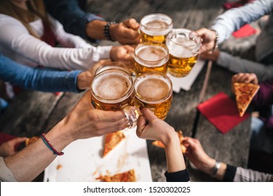 Group of young people having lunch on a terrace of an apartment - Millennials having fun together on a day of celebration - Toast with mugs of beer - Powered by Shutterstock