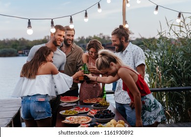 Group Of Young People Having Outdoor Dinner Party By The River.