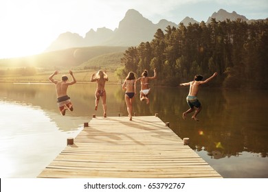 Group of young people jumping into the water from a jetty. Group of friends jumping from pier in the lake on a sunny day. - Powered by Shutterstock