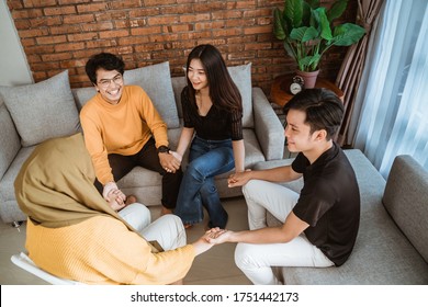 Gruppe junger Menschen, die zusammen lachen und Hände mit Freunden im Zimmer sitzen