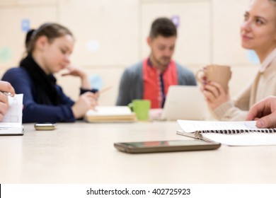 Group of young People male and female Students sitting at wooden Table and doing different Leisure activities reading writing drinking working dreaming