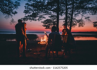 Group of young people near camp fire , telling stories near the fire with wood, flames in the nature at night near lake. - Powered by Shutterstock