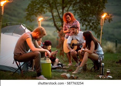 Group Of Young People At Night In Campground Look At Photos On Mobile