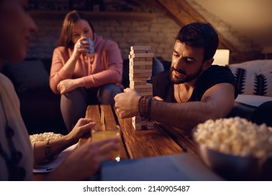 Group Of Young People Playing Jenga While Relaxing In The Evening At Home. Focus Is On Man.