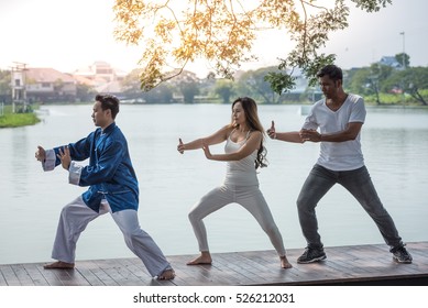 Group of young people practicing traditional Tai Chi Chuan, Tai Ji  and Qi Gong for fighting match together in the park on the lake background, traditional chinese martial arts concept.