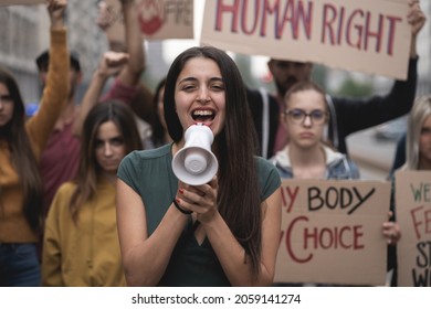 Group of young people protesting on the street with signs raised to promote women rights and right to abortion. Focus on the woman in front screaming to the megaphone - Shutterstock ID 2059141274