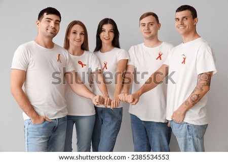 Group of young people with red ribbons putting hands together on grey background. World AIDS day concept