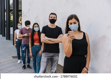 Group of young people at safety distance near a white wall in queue in protection by Coronavirus, Covid-19 with face mask while using the device - Multiracial group of friends - Concept of security