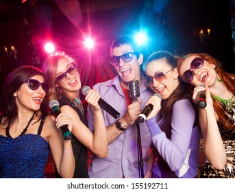  Group Of Young People Singing Into  Microphone At  Party. Karaoke