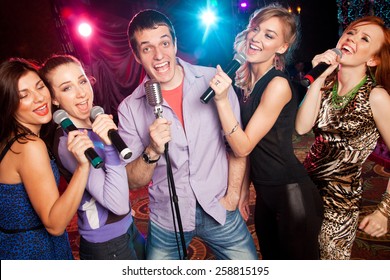 Group Of Young People Singing Into  Microphone At  Party. Karaoke