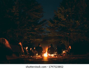 The group of young people are sitting around the bonfire and talking and singing songs - Shutterstock ID 1797523852