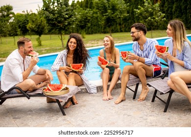 Group of young people sitting by the swimming pool and eating watermelon in the house backyard